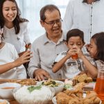 A family gathering around a table to share a meal together during the holidays. They’re smiling as a young boy digs in first.