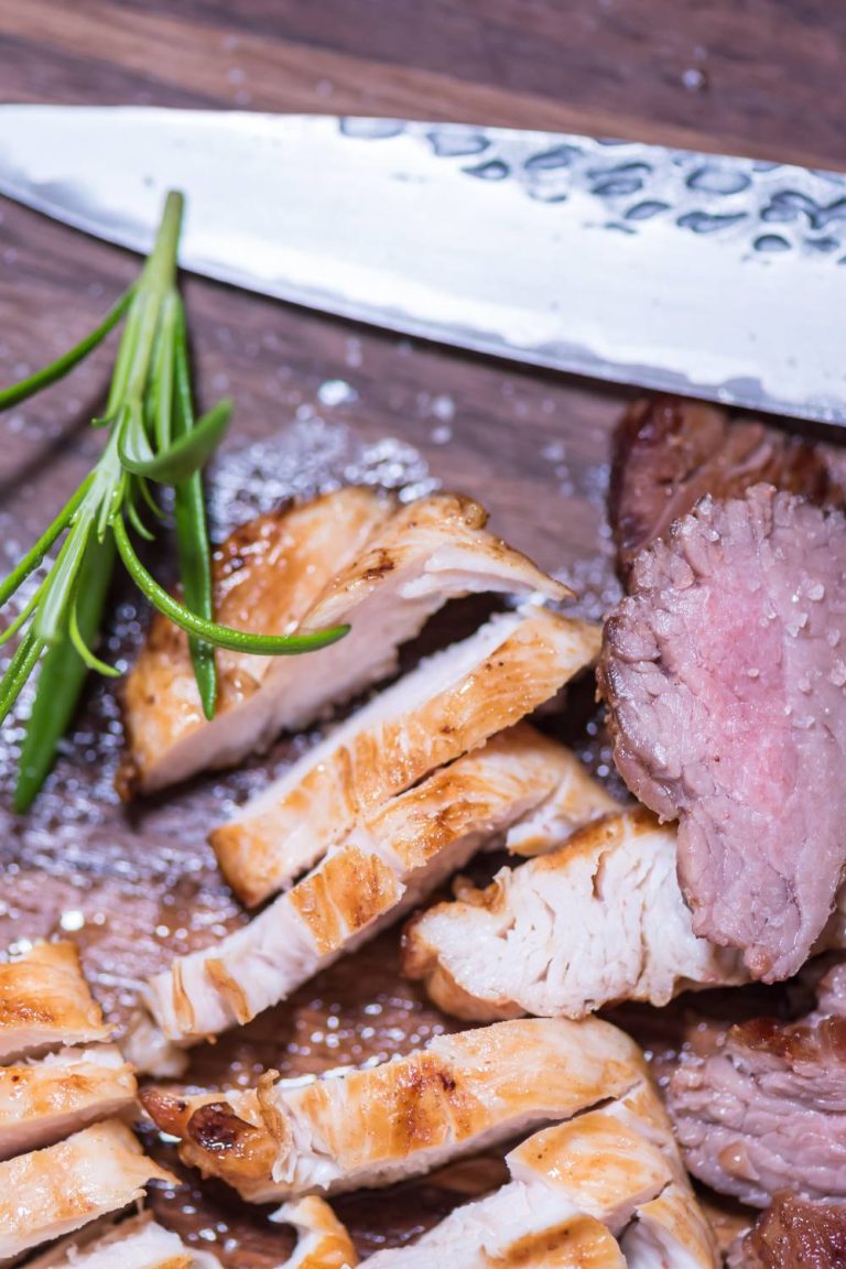 A wooden platter with a large knife and a variety of meats such as steak and chicken. There's a garnish on the platter.