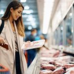 A happy woman buys meat at the refrigerated section in the supermarket. She's inspecting the red meat.
