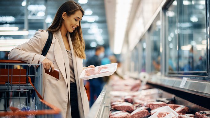 A happy woman buys meat at the refrigerated section in the supermarket. She's inspecting the red meat.